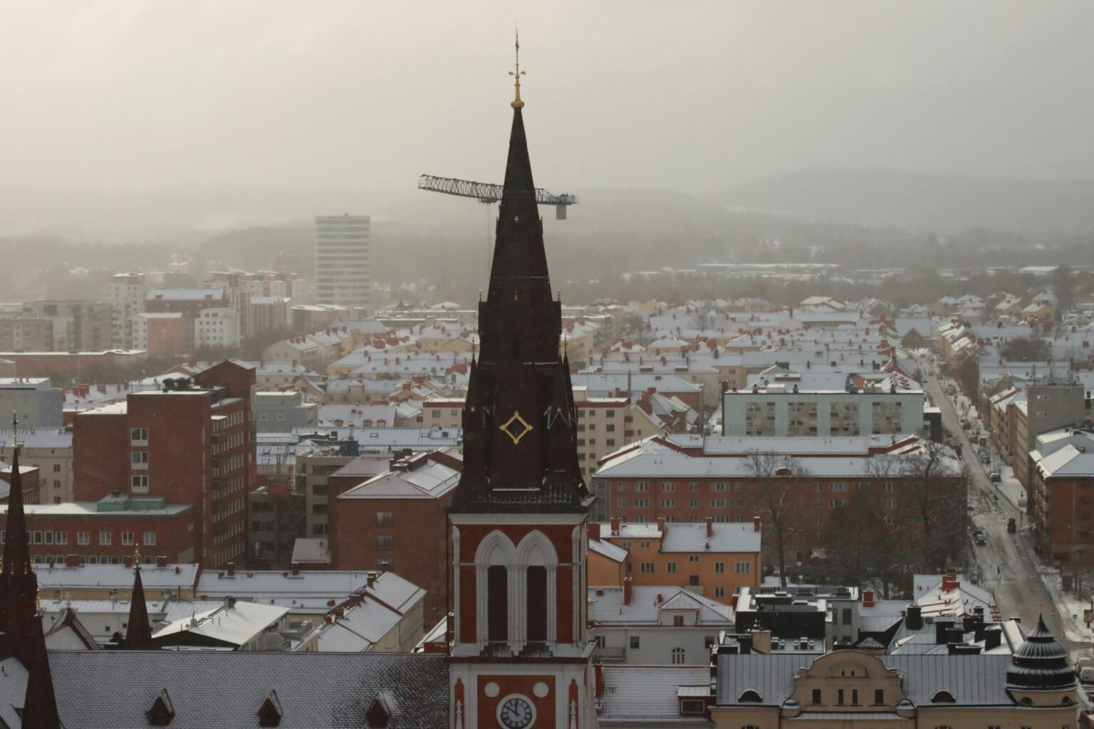 Aerial view of a snowy city with a prominent church spire during winter.